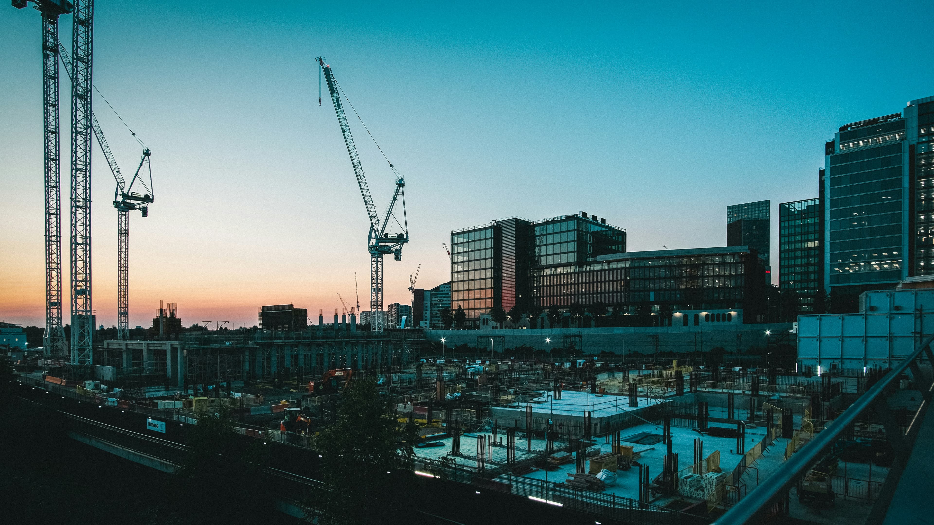 Construction site at low sun, cranes over concrete foundations
